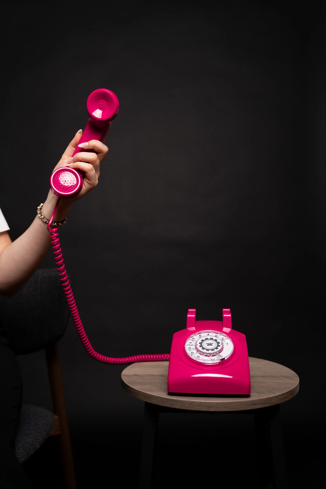 Hand hält den Hörer eines pinkfarbenen Wählscheibentelefons – stilvolles Symbol für direkte Kommunikationsberatung – auf einem Holztisch vor dunklem Hintergrund.
