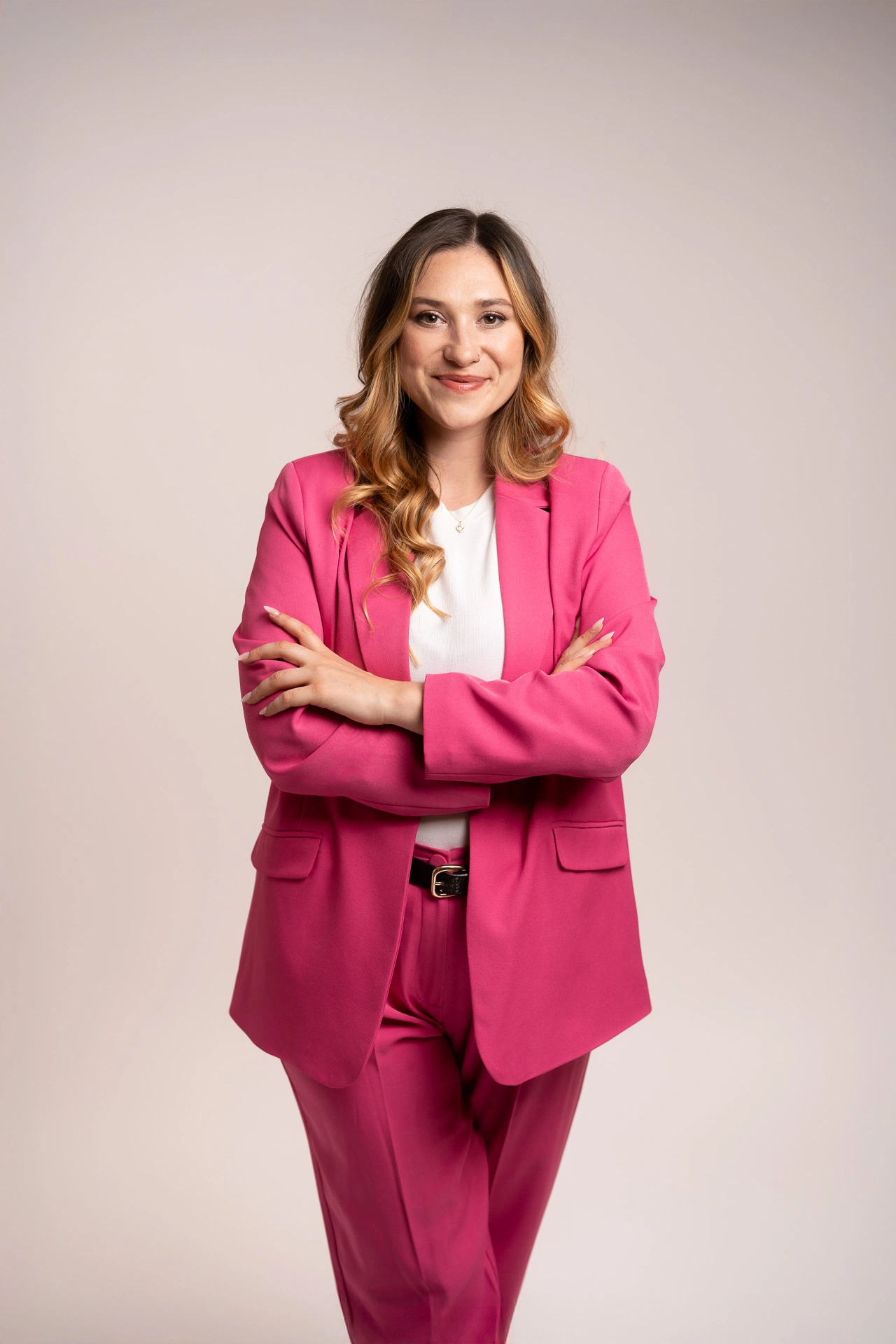 Lucia, Gründerin von Better Call Lucy und Expertin für Öffentlichkeitsarbeit, im Business-Anzug mit verschränkten Armen, lächelt selbstbewusst in die Kamera. Ihre langen, braunen Locken fallen über die Schultern. Schwarzer Hintergrund.