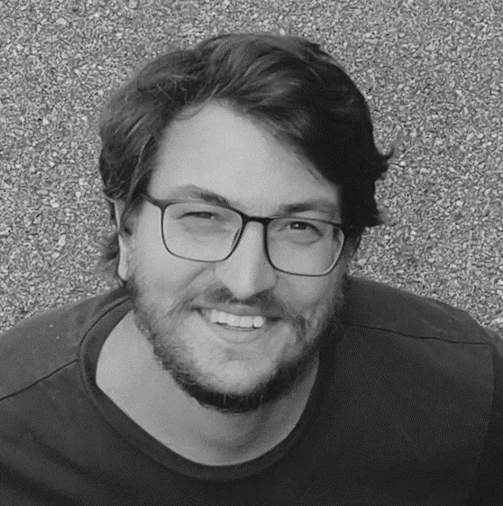 Florian Walter, zuständig für Öffentlichkeitsarbeit beim Schlachthof Wels, auf einem Schwarz-Weiß-Porträt. Er trägt ein legeres T-Shirt, kurze glatte Haare, einen kurzen Bart und eine Brille. Er lächelt freundlich von unten nach oben in die Kamera.